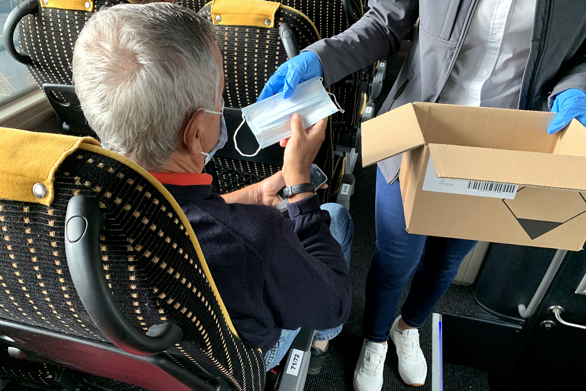 A képen a volánbusz dolgozója egy maszkot ad át egy utasnak a fedélzeten.
