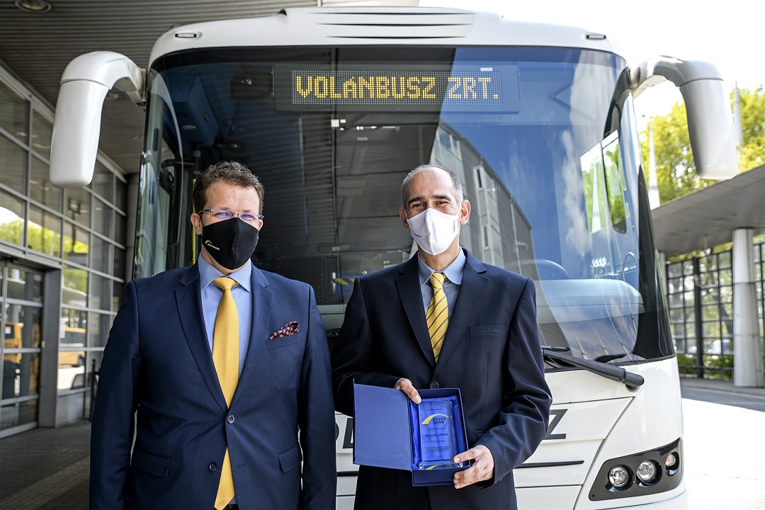 A képen Pafféri Zoltán elnök-vezérigazgató és Boros János autóbusz-vezető látható egy fehér autóbusz előtt a Népliget autóbusz-állomáson. Boros János a kezében az Érték Rend díjat tartja.