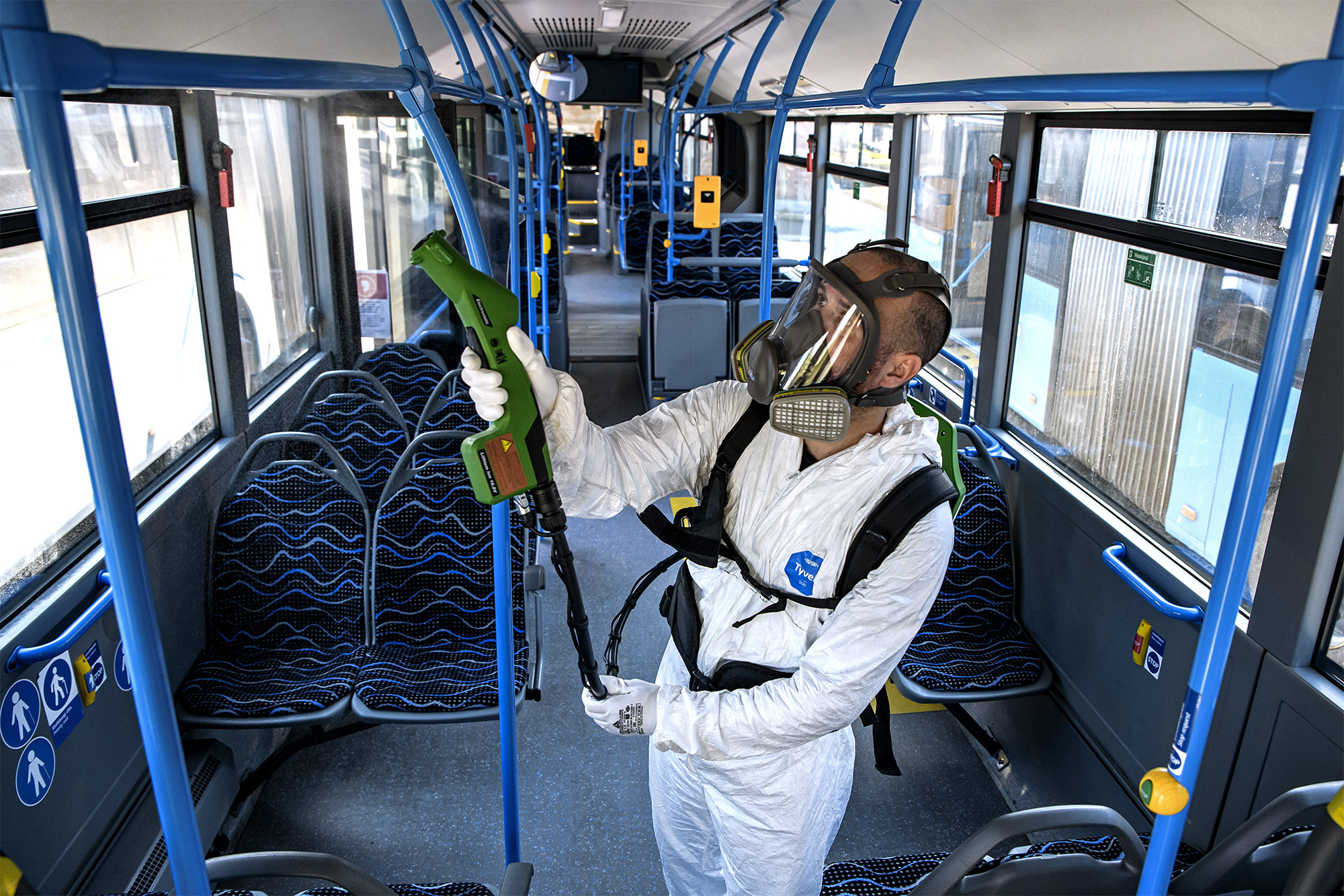 A képen egy védőruhás szakember látható a busz belsejének tisztítása közben.