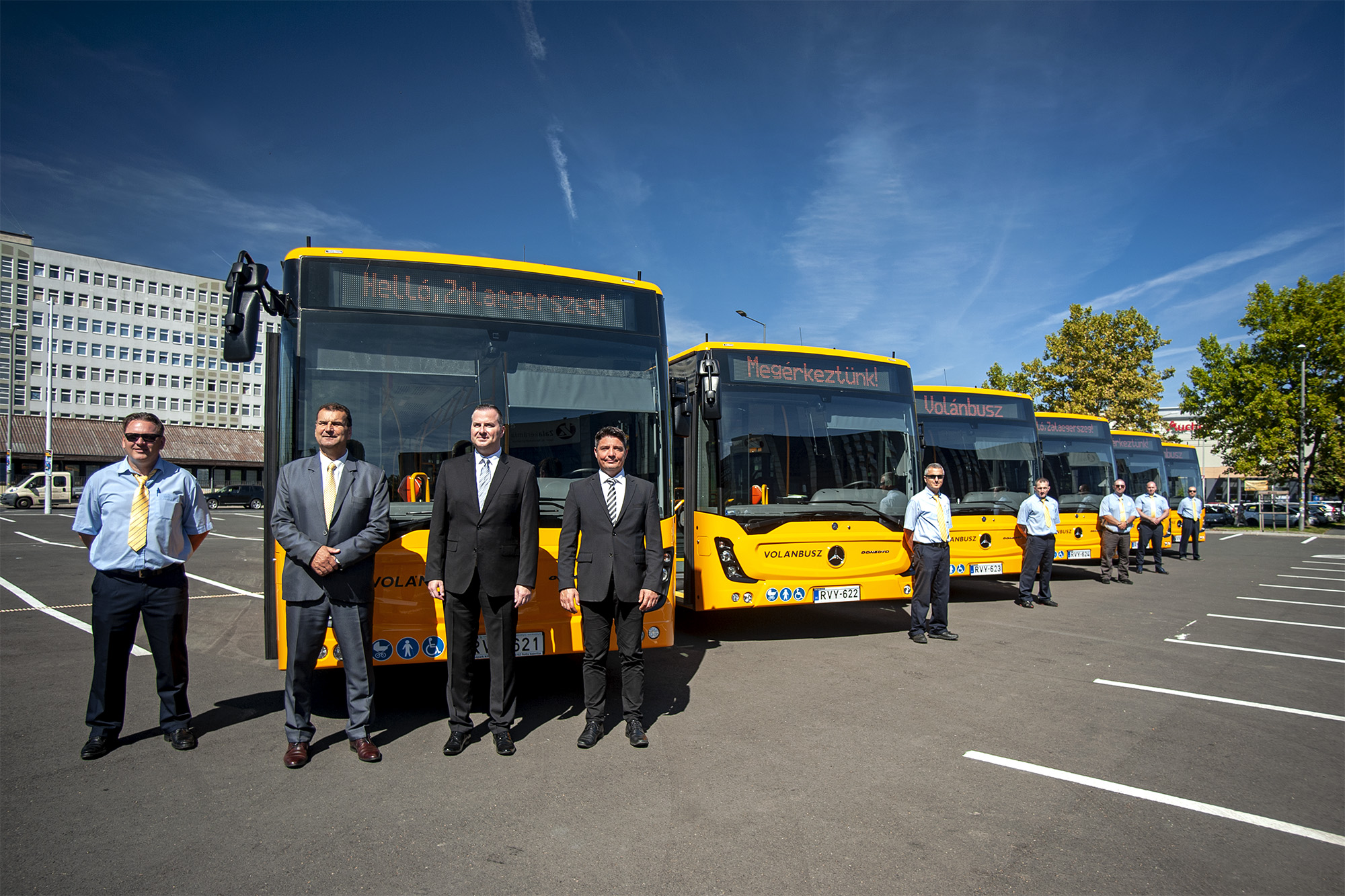 A képen a sajtótájékoztatón részvevők, valamint az autóbuszsofőrök az autóbuszaik mellett láthatók.