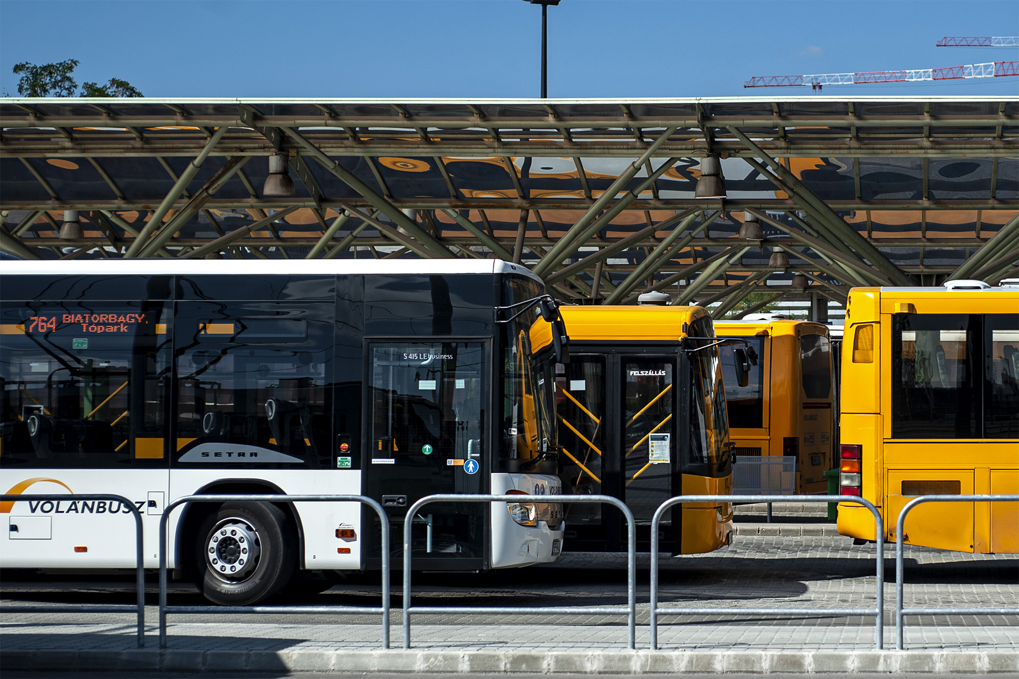 A képen oldalról fotózott autóbuszok láthatók egy autóbusz állomáson.
